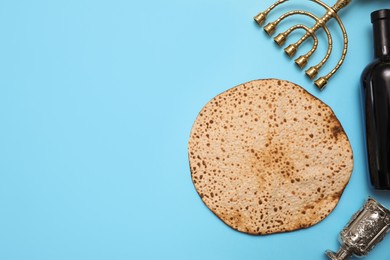 Photo of Tasty matzo, wine and menorah on light blue background, flat lay with space for text. Passover (Pesach) celebration