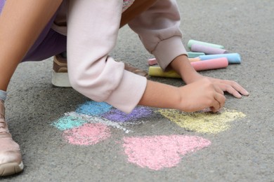 Photo of Little child drawing butterfly and hearts with chalk on asphalt, closeup