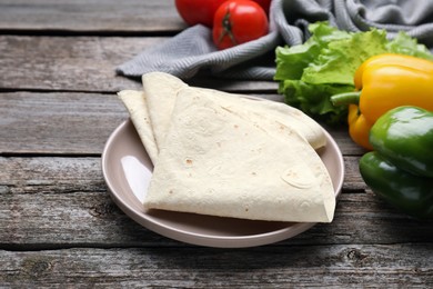 Photo of Delicious folded Armenian lavash and fresh vegetables on wooden table