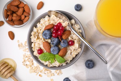 Photo of Oatmeal served with berries, almonds and honey on white table, flat lay