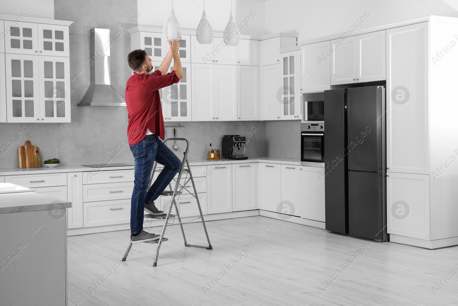 Photo of Young man installing ceiling lamp on stepladder in kitchen, space for text