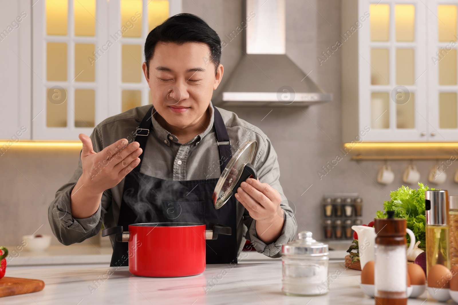 Photo of Man with pot smelling dish after cooking at countertop in kitchen