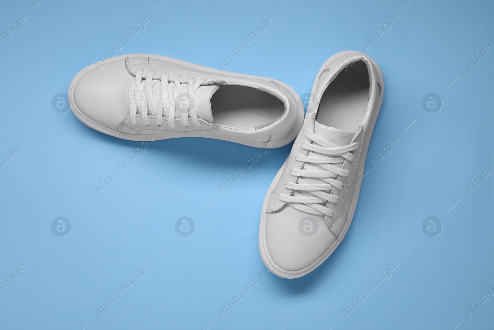 Photo of Pair of stylish white sneakers on light blue background, top view