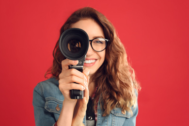 Photo of Beautiful young woman with vintage video camera against red background, focus on lens