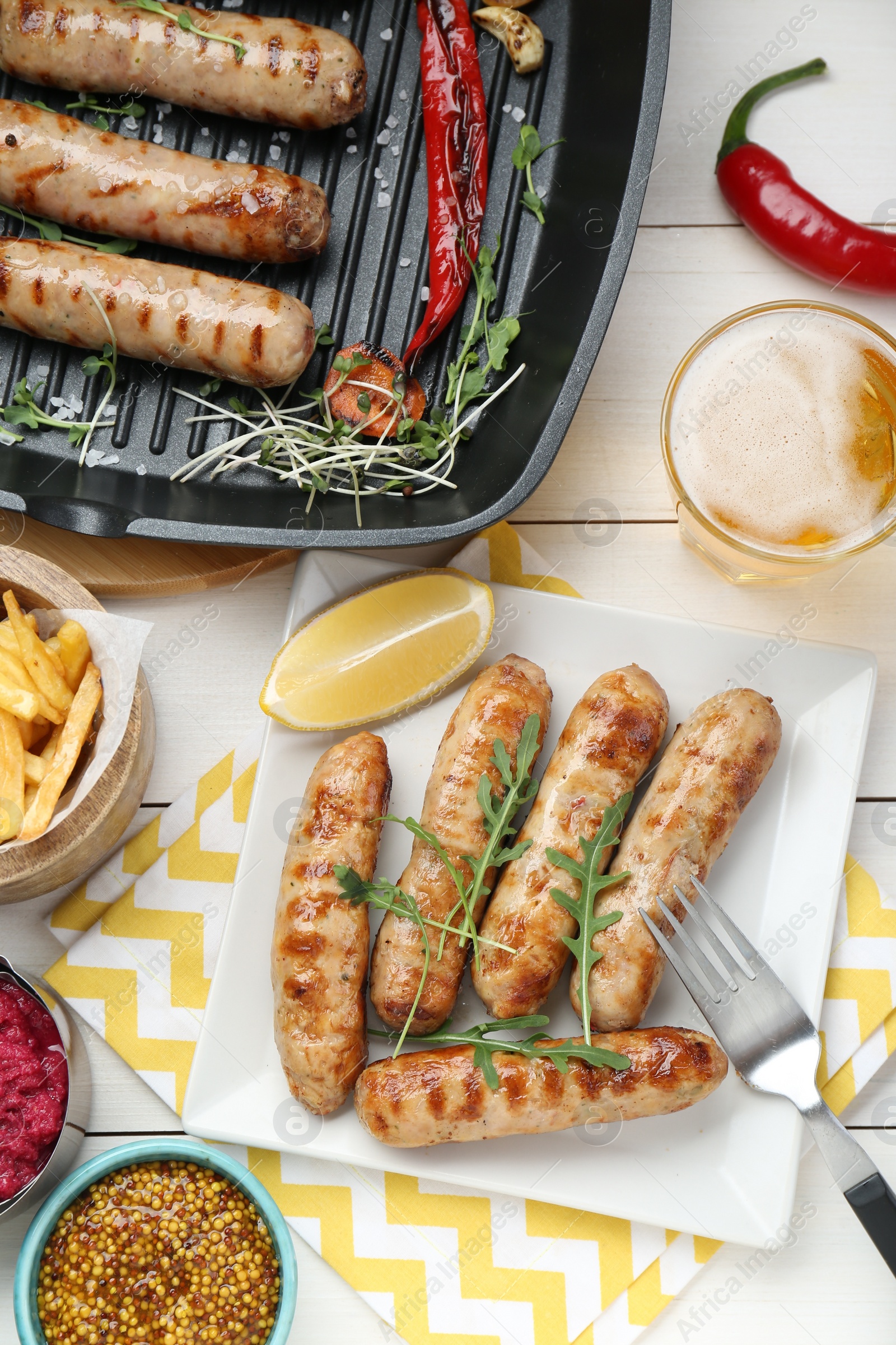 Photo of Tasty grilled sausages served on white wooden table, flat lay