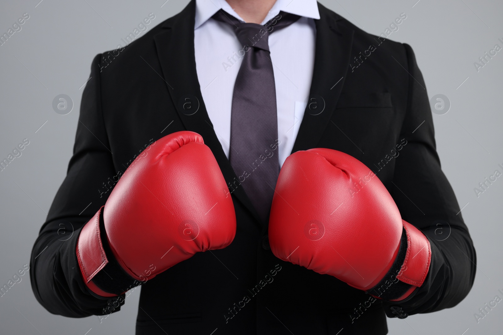 Photo of Businessman in suit wearing boxing gloves on grey background, closeup