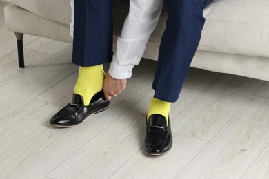 Photo of Man with yellow socks putting on stylish shoes indoors, closeup