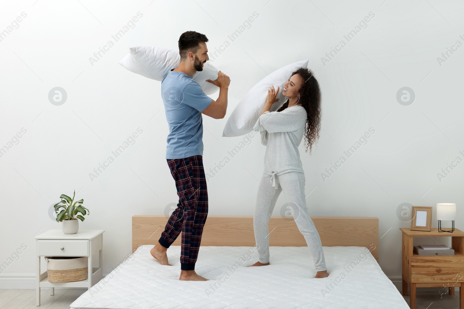 Photo of Happy couple having pillow fight on bed with comfortable mattress at home