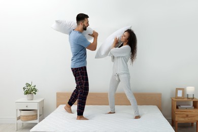 Photo of Happy couple having pillow fight on bed with comfortable mattress at home