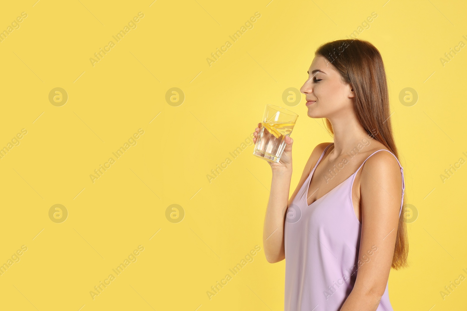 Photo of Young woman drinking lemon water on yellow background. Space for text