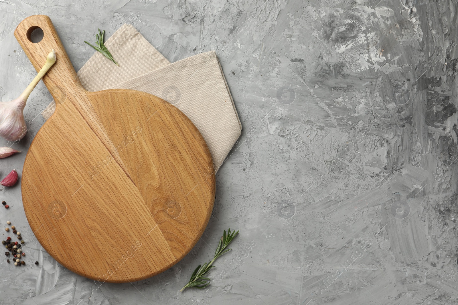 Photo of Cutting board, garlic, spices and rosemary on grey textured table, flat lay. Space for text