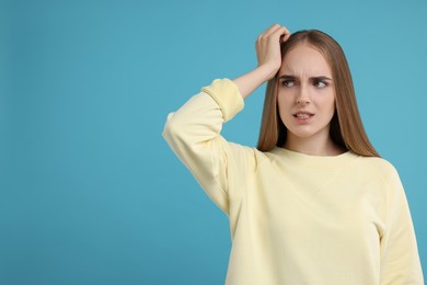 Portrait of embarrassed young woman on light blue background, space for text