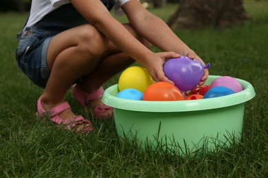 Photo of Little girl with basin of water bombs on green grass, closeup