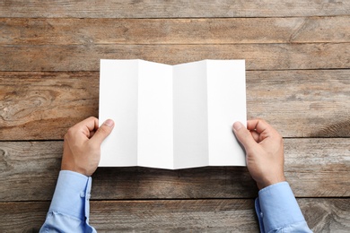 Photo of Young man holding blank brochure at wooden table, top view. Mock up for design