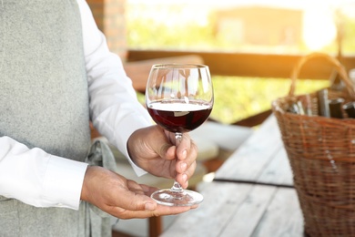 Photo of Waiter holding glass of red wine in outdoor cafe, closeup