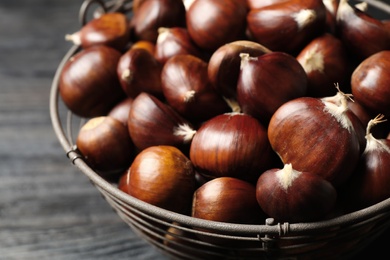 Photo of Fresh sweet edible chestnuts in basket on black table, closeup