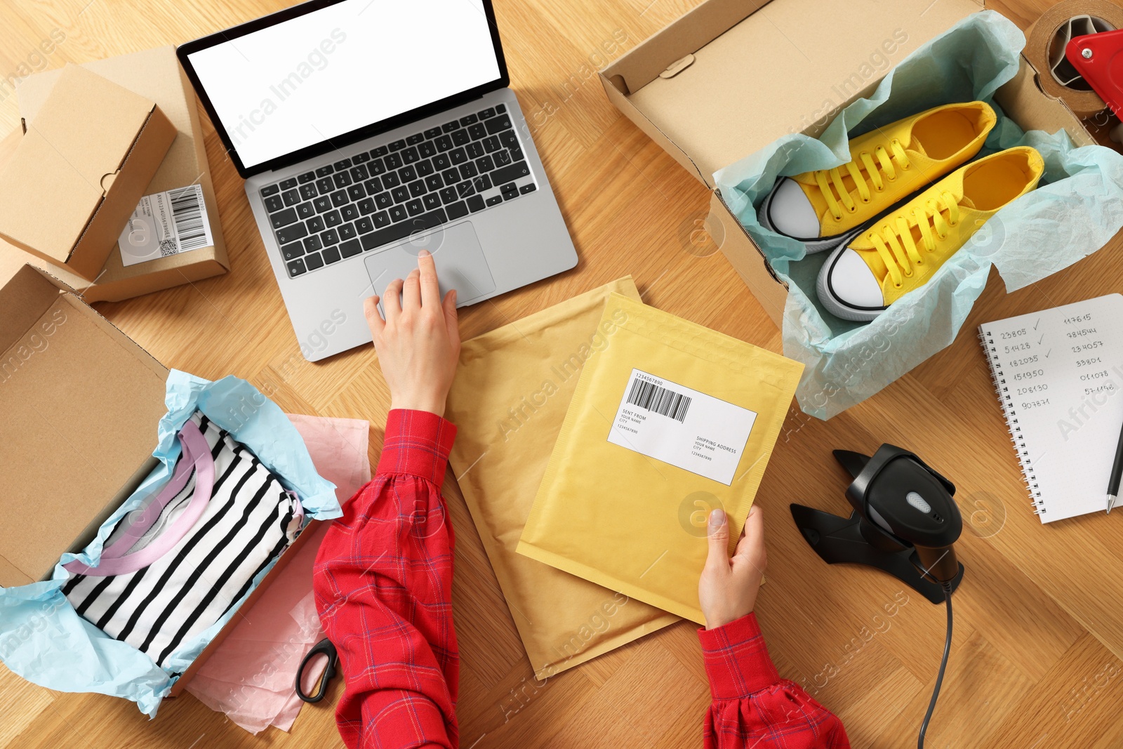 Photo of Woman with laptop and parcel working at wooden table, top view. Online store