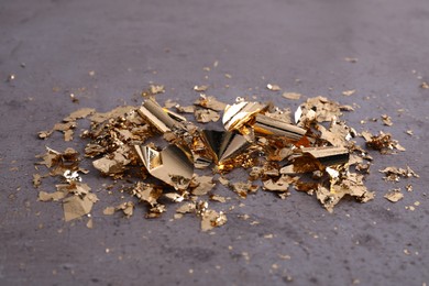 Many pieces of edible gold leaf on grey textured table, closeup