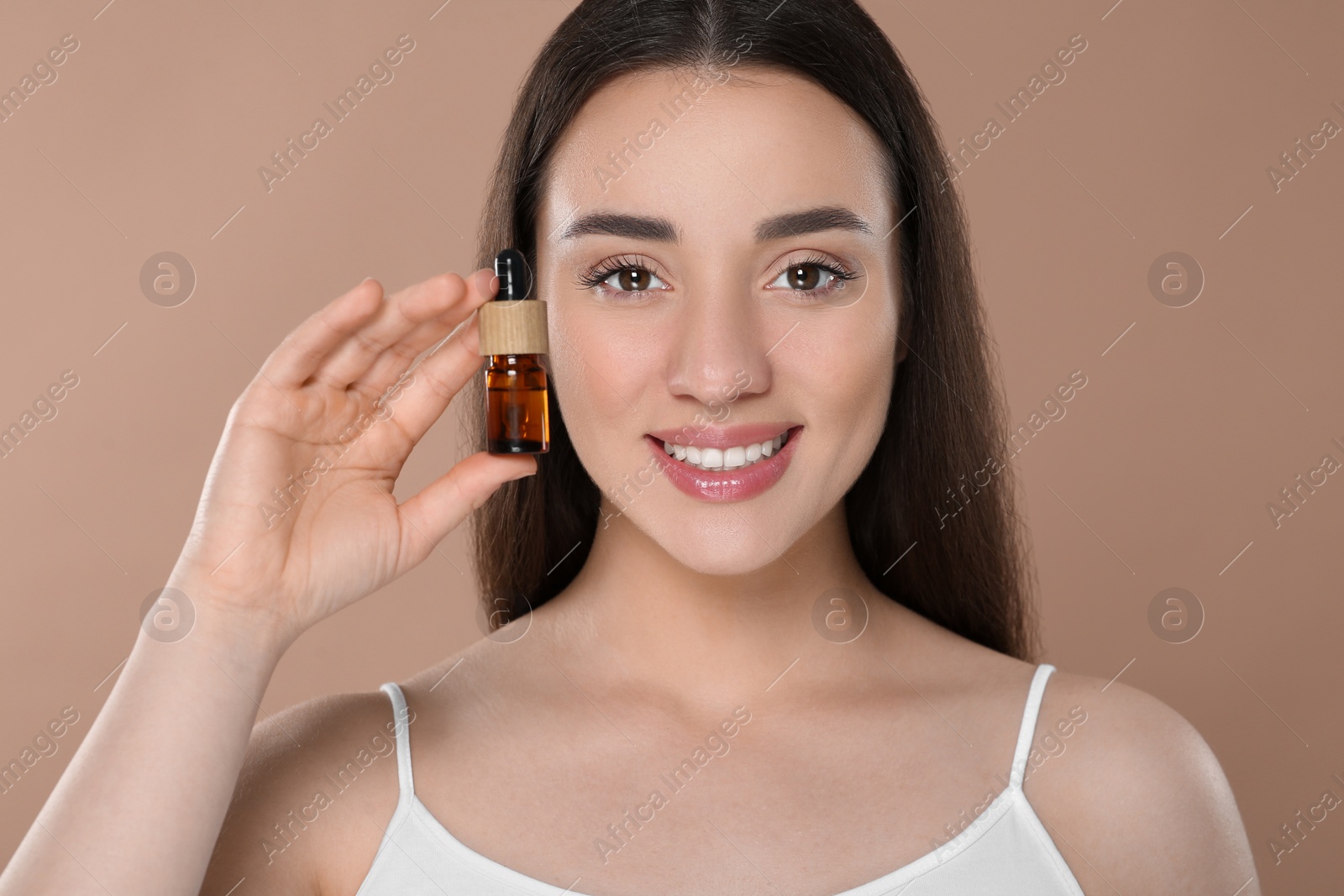 Photo of Beautiful young woman with bottle of essential oil on brown background