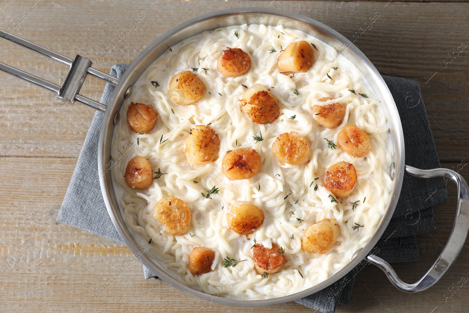 Photo of Delicious scallop pasta in pan on wooden table, top view