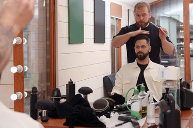 Photo of Professional hairdresser working with bearded client in barbershop