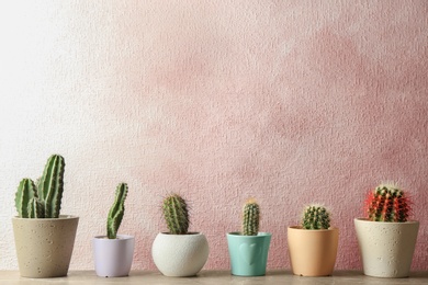 Different potted cacti on table near color background, space for text. Interior decor