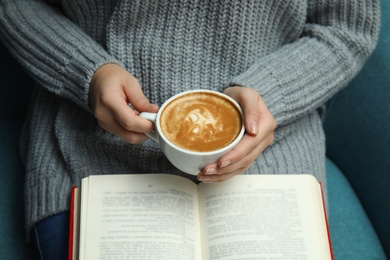 Photo of Woman with cup of coffee reading book at home, closeup