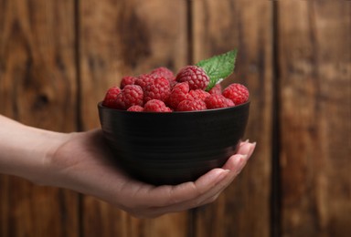 Photo of Woman holding bowl with fresh ripe raspberries against wooden background, closeup