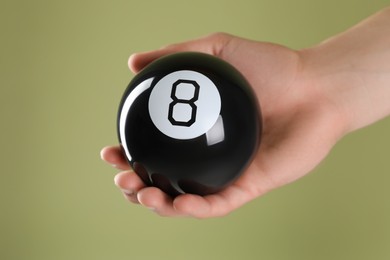 Man holding magic eight ball on olive background, closeup