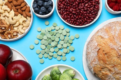 Many prebiotic pills and food on light blue background, flat lay