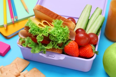 Photo of Lunchbox with tasty food and school stationery on light blue background, closeup