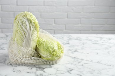 Fresh Chinese cabbages in string bag on white marble table near brick wall. Space for text