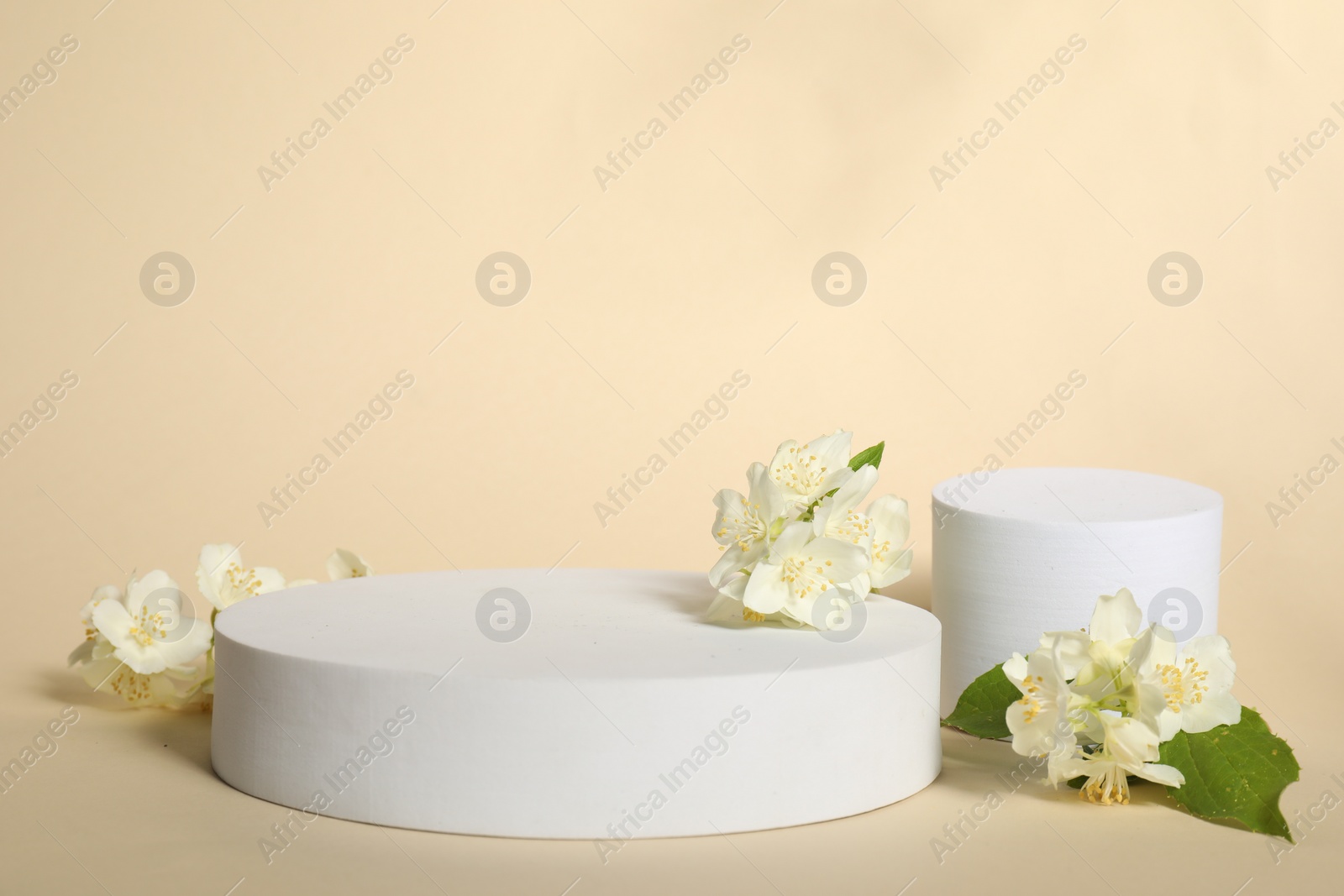 Photo of Presentation of product. White podiums and beautiful jasmine flowers on beige background, space for text