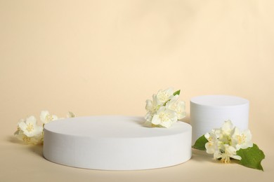 Presentation of product. White podiums and beautiful jasmine flowers on beige background, space for text