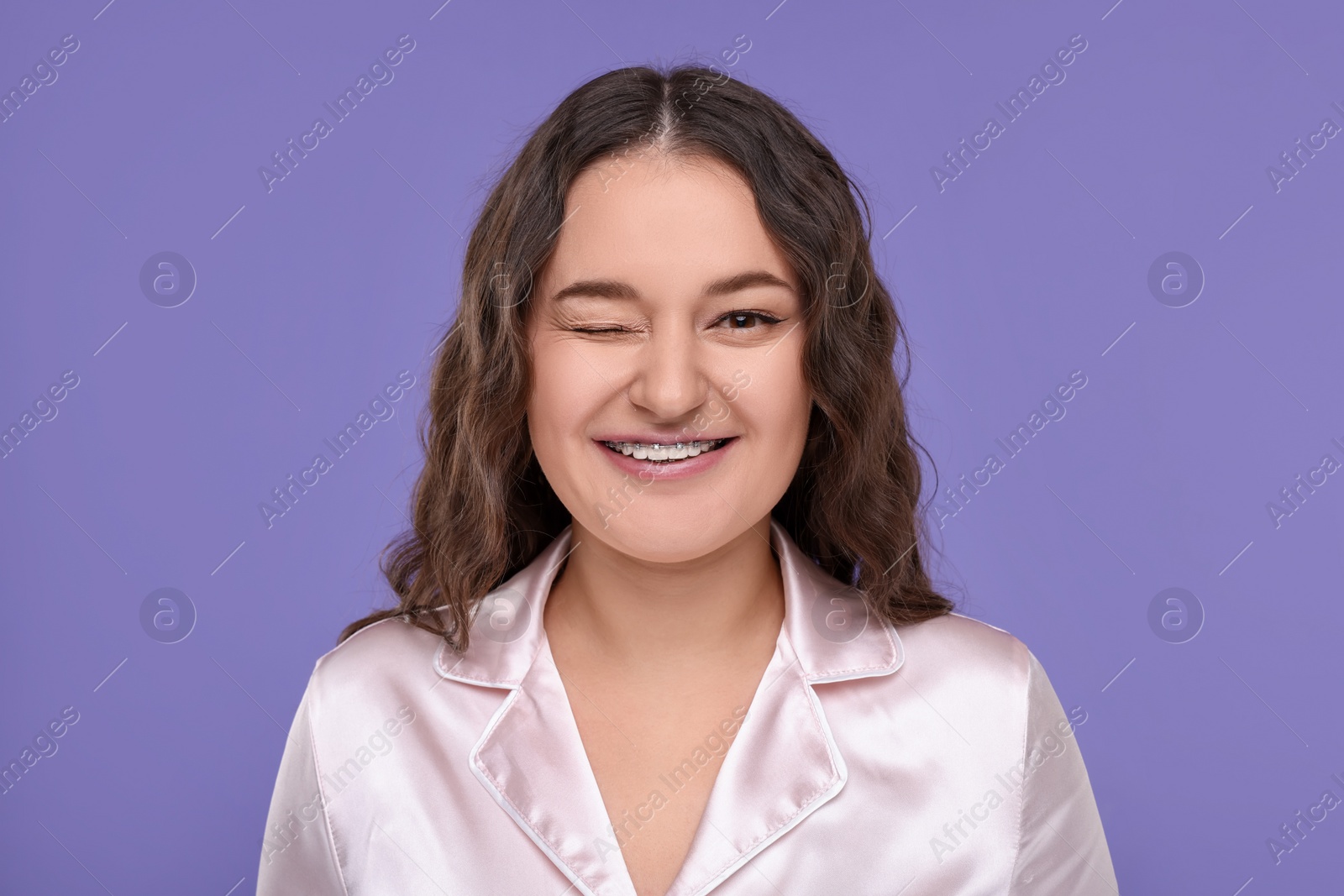 Photo of Smiling woman with braces winking on violet background