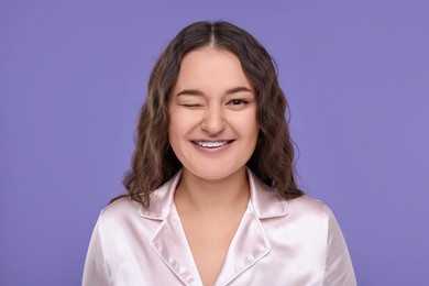 Photo of Smiling woman with braces winking on violet background