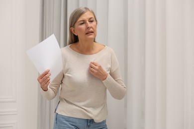 Menopause. Woman waving paper sheet to cool herself during hot flash at home, space for text