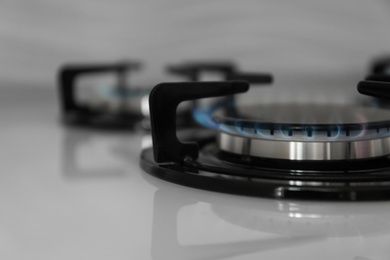 Photo of Gas burner with blue flame on modern stove, closeup. Space for text