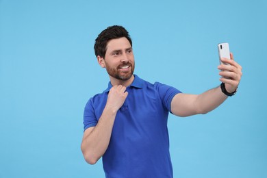 Smiling man taking selfie with smartphone on light blue background