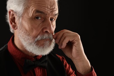 Senior man touching mustache on black background