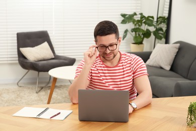 Photo of Man working with laptop at wooden table in room