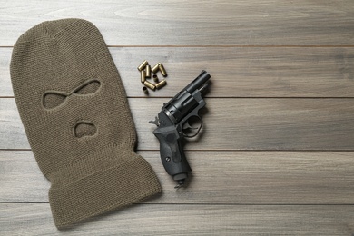 Photo of Balaclava, pistol and bullets on wooden table, flat lay. Space for text