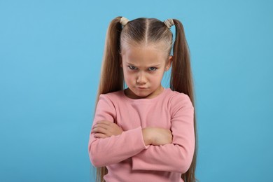 Photo of Resentful girl with crossed arms on light blue background