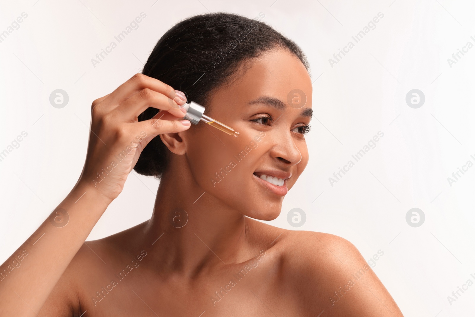 Photo of Smiling woman applying serum onto her face on white background