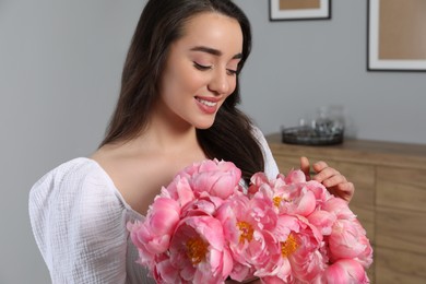 Photo of Beautiful young woman with bouquet of pink peonies at home