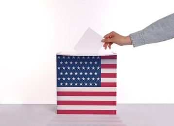 Image of Woman putting her vote into ballot box decorated with flag of USA against white background, closeup