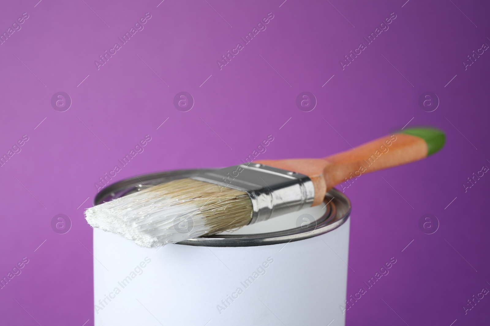 Photo of Can of white paint with brush on purple background