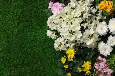 Different beautiful flowers on green grass, flat lay. Space for text