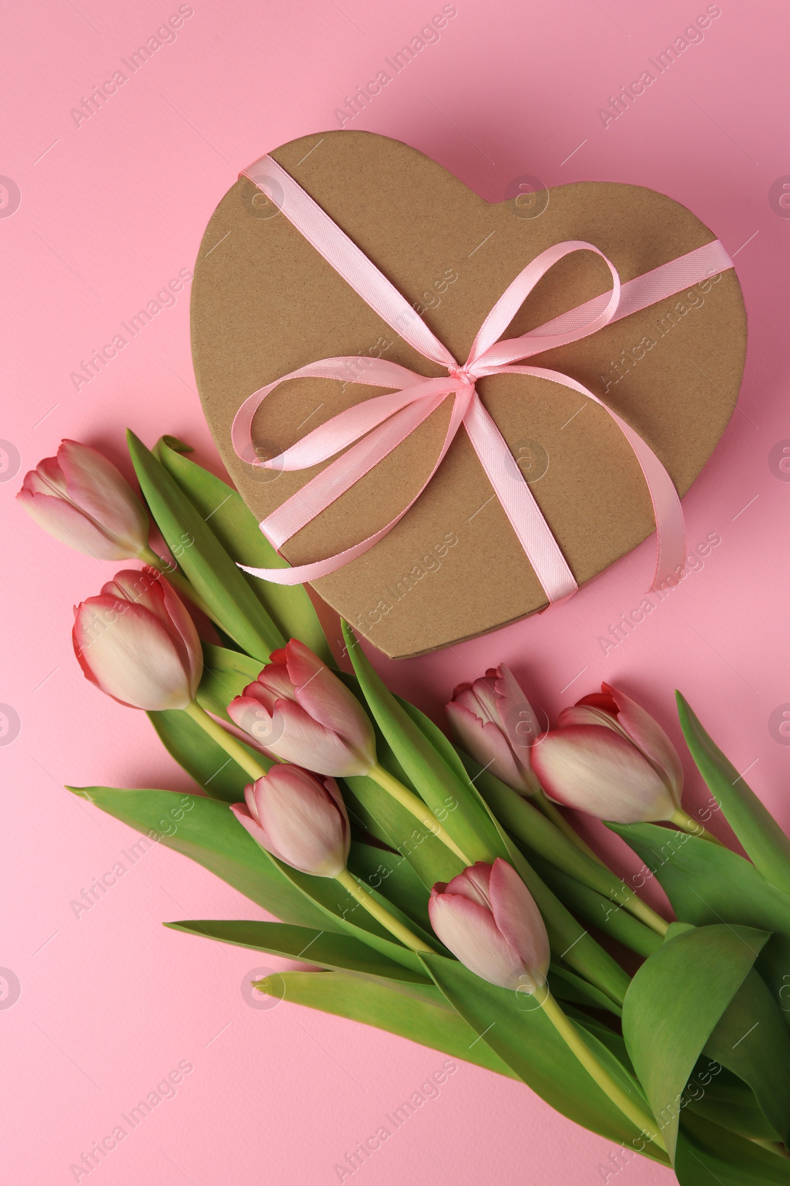 Photo of Heart shaped gift box with bow and beautiful tulips on pale pink background, flat lay