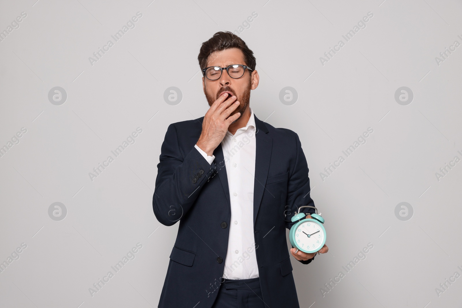 Photo of Sleepy bearded man with alarm clock on light grey background